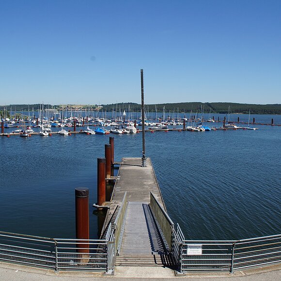 Der Seglhafen am Brombachsee. Ins Wasser führt ein schmaler Steg. Dahinter liegt etwas entfernt der Segelhafen mit vielen Segelbooten.
