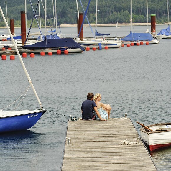 Segelhafen Auf dem Steg des Ramsbergers Segelhafens am Brombachsee genießen zwei Verliebte die wunderschöne Aussicht auf den Brombachsee und die Segelschiffe.