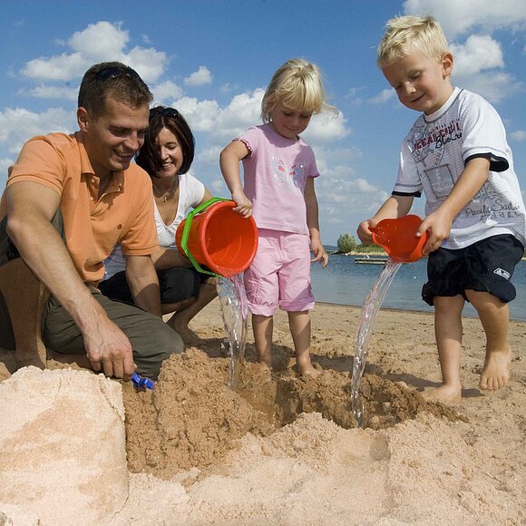 Badestrand Eine vierköpfige Familie spielt am Strand des Brombachsees in Ramsberg. Die zwei Kinder erfreuen sich am sandeln und genießen die Zeit.