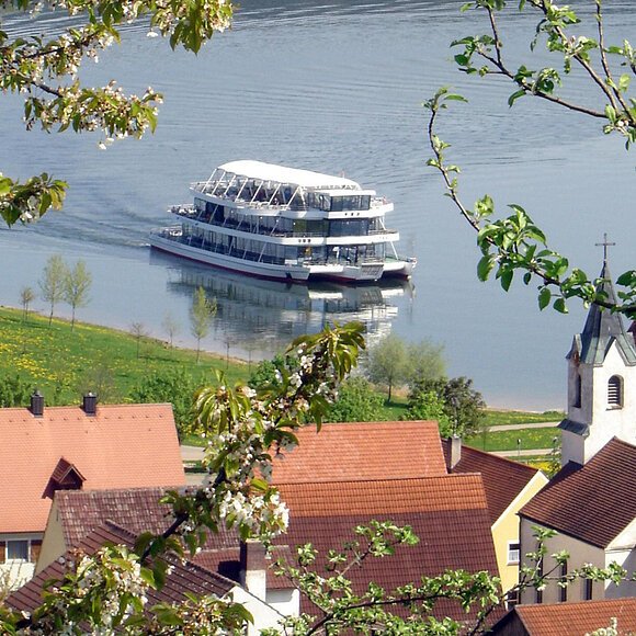 Eine Runde Schifffahren am Brombachsee Blick von einer erhebung auf einen See. Darauf fährt ein großes Personenschiff in der Nähe des grünen Ufers entlang. Am See eine Wohnsiedlung.