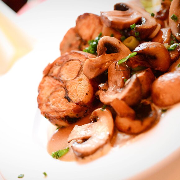 Nahaufnahme eines Pilzgerichtes. Gebratene Champigons dazu Semmelknödel platziert auf einem weißen Teller.