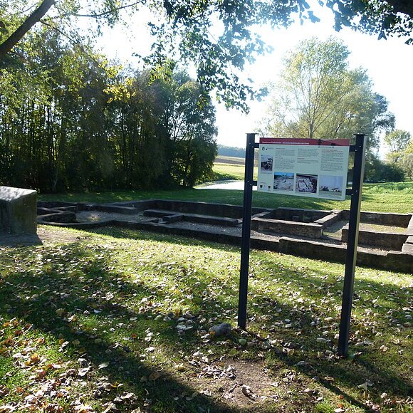 Römische Ruine Eine römische Ruine auf einer grünen Wiese. Davor steht eine Infotafel.